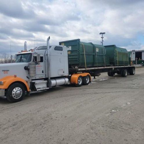 A semi truck with a green dumpster on the back is parked in a dirt lot