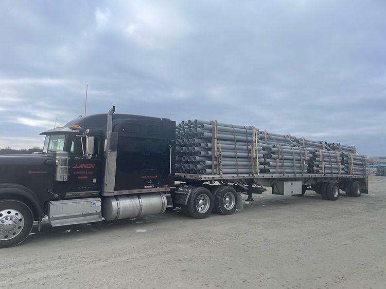 A semi truck is carrying a trailer full of pipes