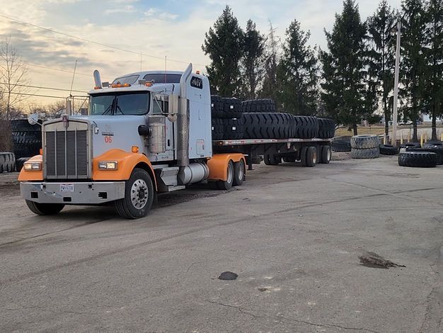 A semi truck is carrying a flatbed trailer filled with tires
