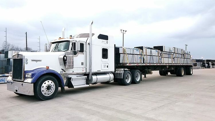 A semi truck with a flatbed trailer is parked in a parking lot