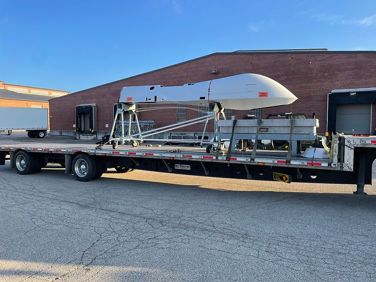 A trailer with a drone on it is parked in front of a brick building