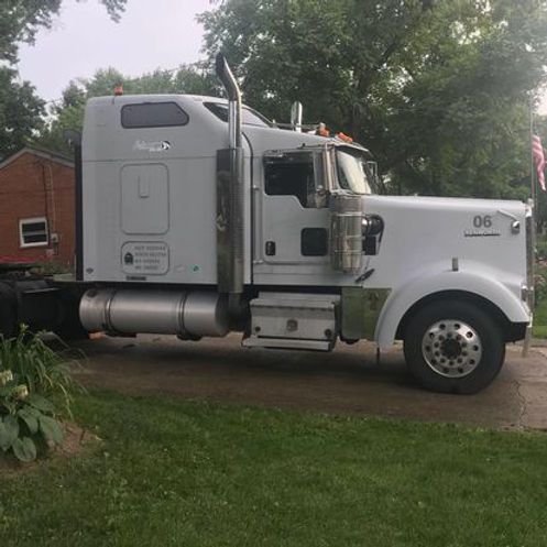 A white semi truck is parked in a driveway next to a brick building
