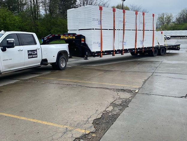 A white truck is towing a trailer with stacks of bricks on it