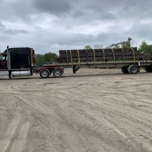 A semi truck is driving down a dirt road with a flatbed trailer