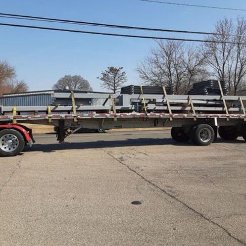 A semi truck with a flatbed trailer is carrying a large load of metal