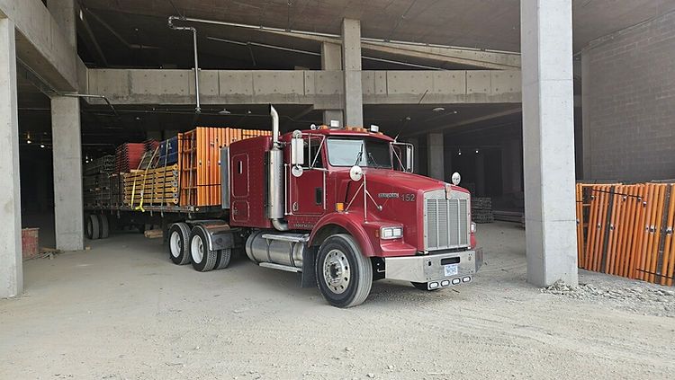 A red semi truck is parked in a building under construction