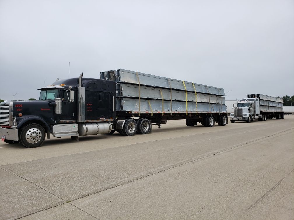 Two semi trucks are driving down a road carrying a large load.