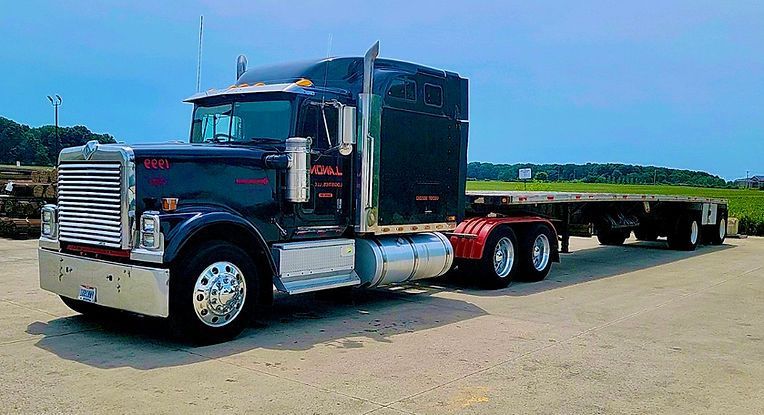 A black semi truck with a flatbed trailer is parked in a gravel lot