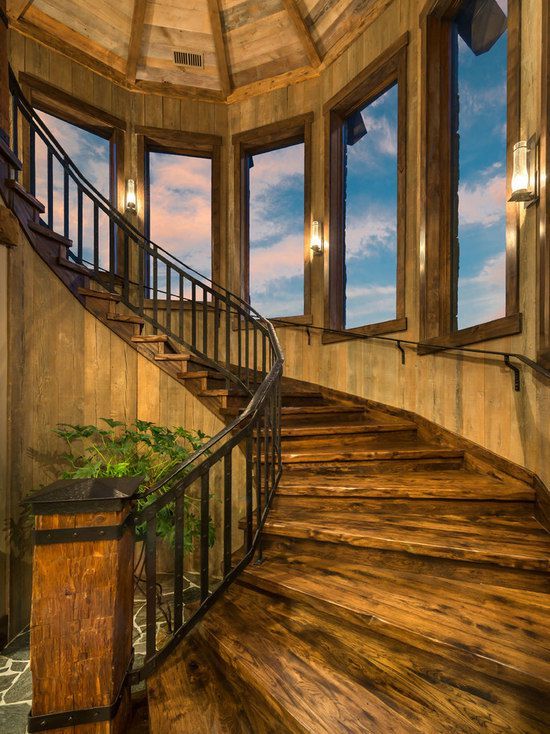 A wooden spiral staircase with a metal railing and lots of windows.