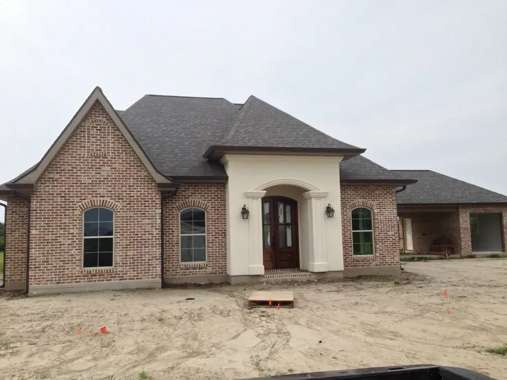 Brick house with a white entryway, brown door, and dark roof under cloudy skies.