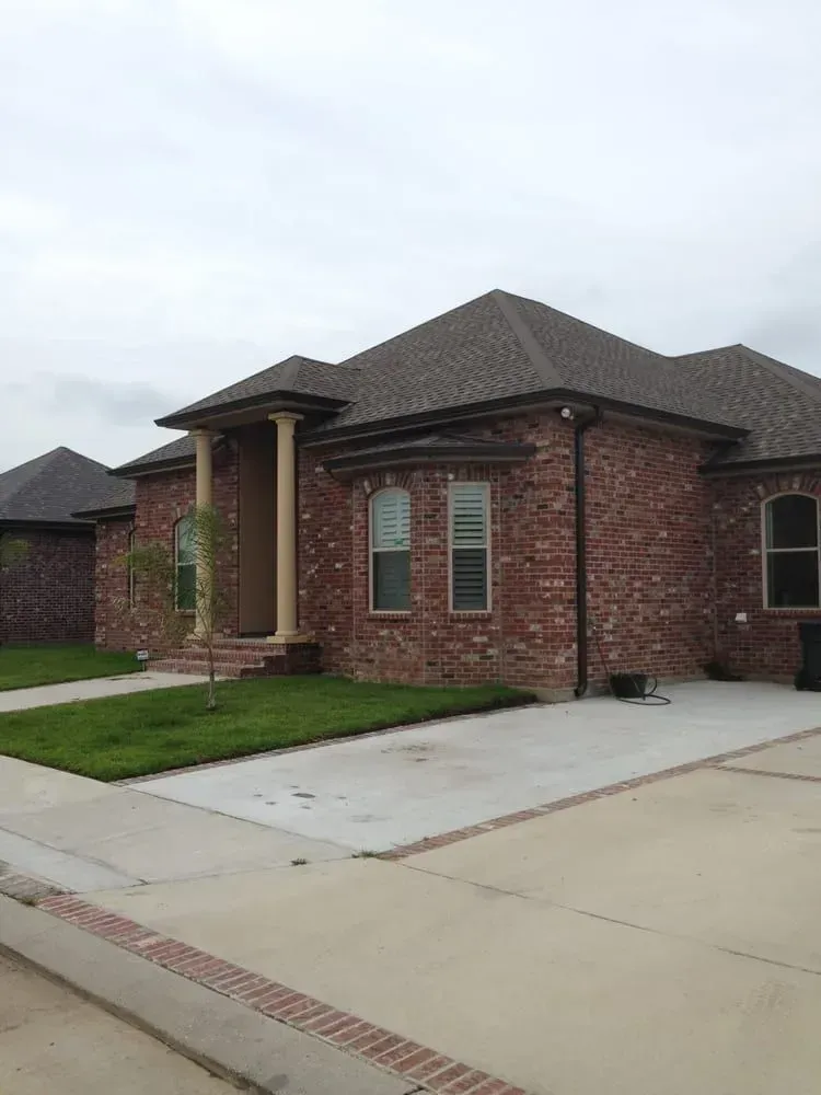 Brick house with a brown roof and a concrete driveway on an overcast day.