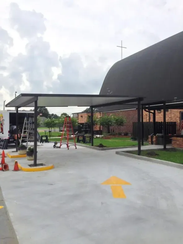 Drive-thru awning with yellow arrow, next to a building with a cross. Construction materials visible. Overcast sky.