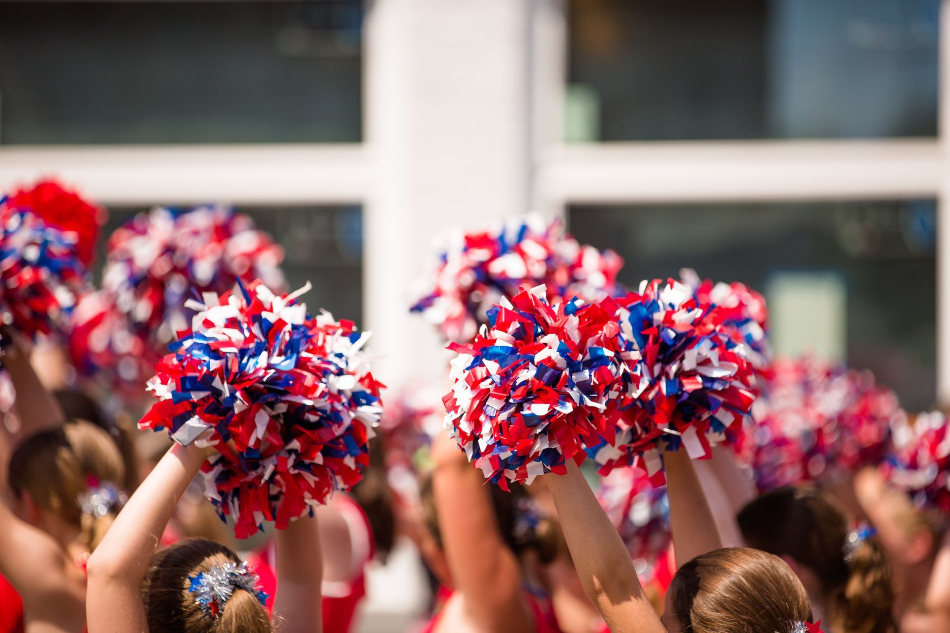 Red, white, and blue pom-poms held high by cheerleaders during a performance.