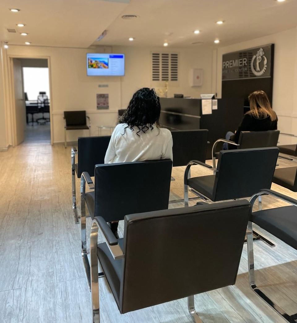 Una mujer se sienta en una sala de espera frente a un cartel que dice