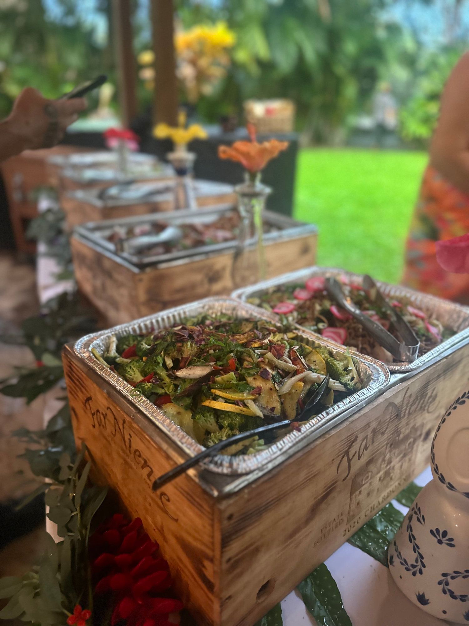 Buffet table with metal serving trays of salad and grilled vegetables outdoors on a green lawn