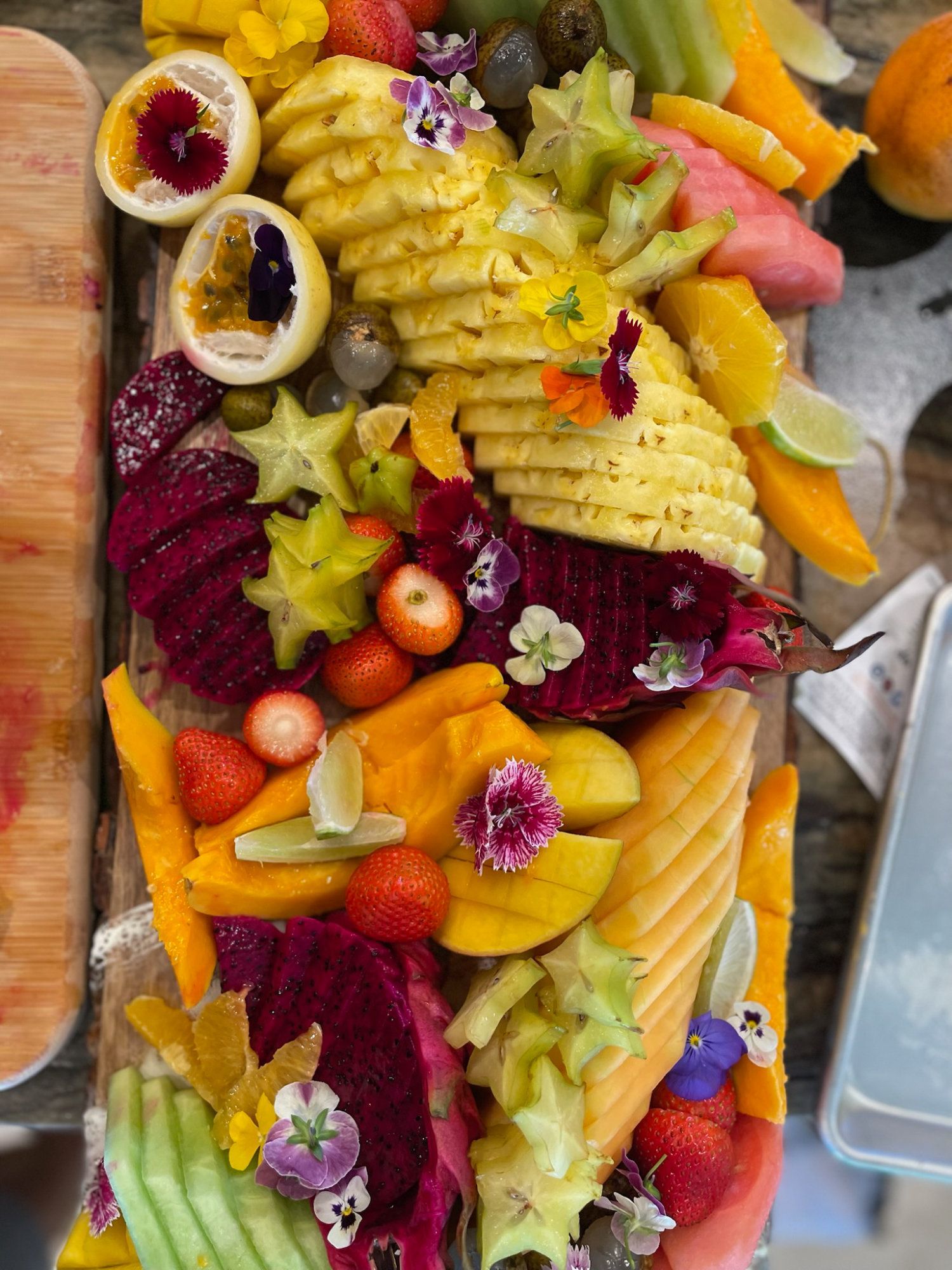 Colorful fruit platter with pineapple, dragon fruit, melon, grapes, kiwi, and berries on a wooden board