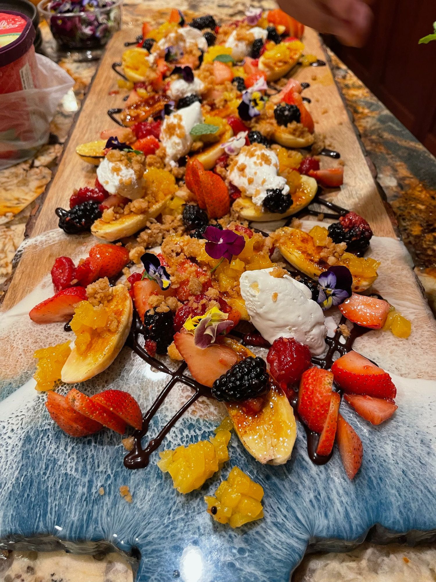 Long dessert board with waffles, strawberries, whipped cream, chocolate drizzle, and flowers