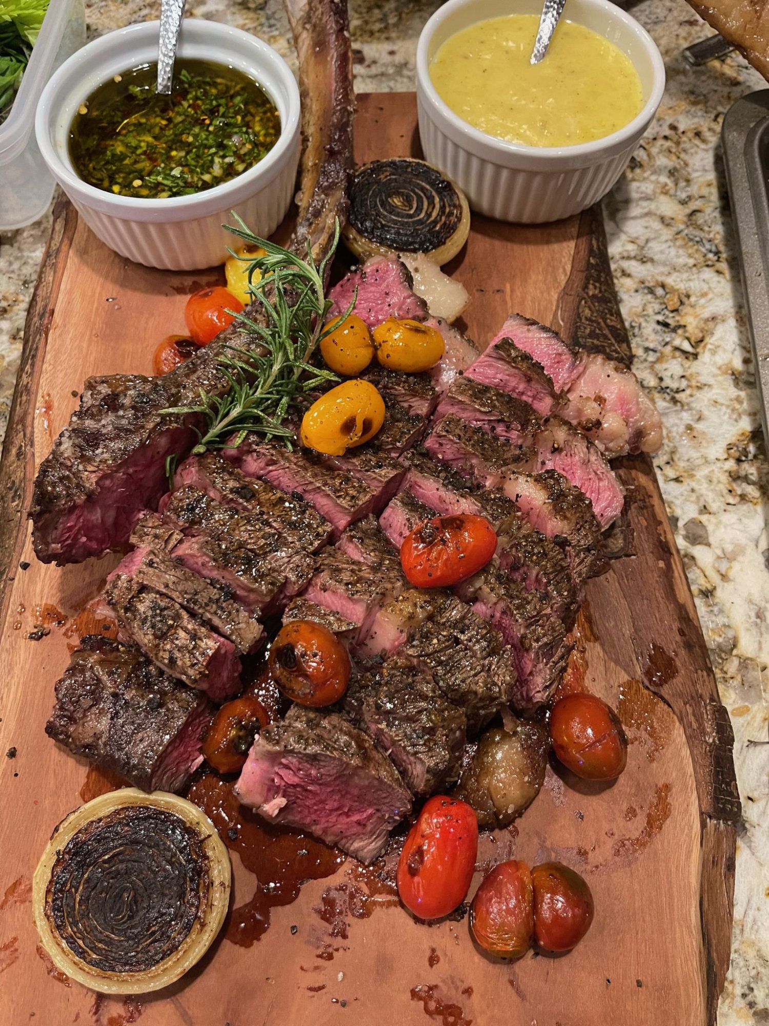 Sliced steak on a wooden board with cherry tomatoes and two dipping sauces in small bowls