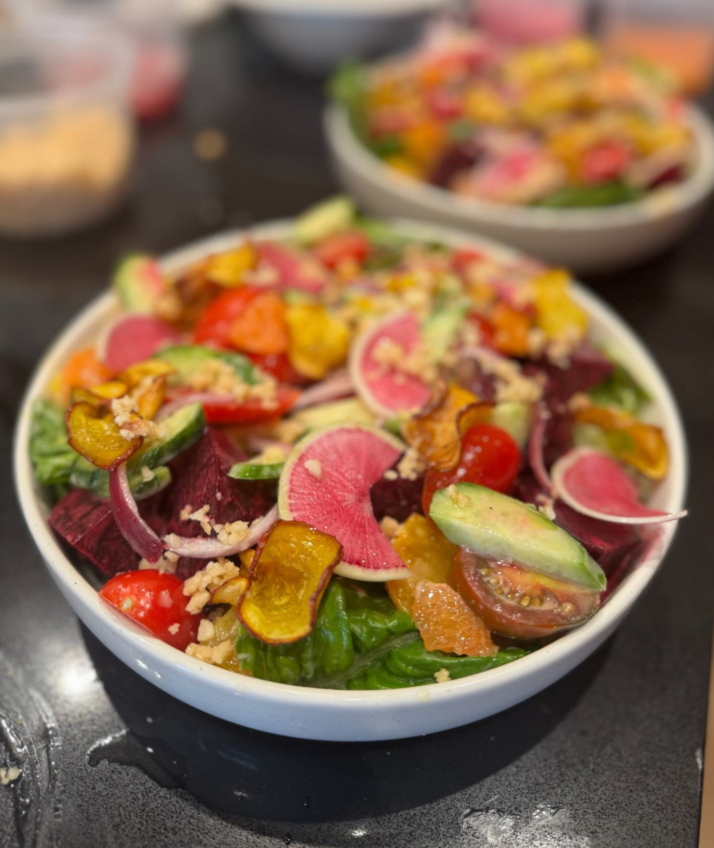 Colorful salad bowls topped with radish slices, cucumber, and yellow and red vegetables on a dark table