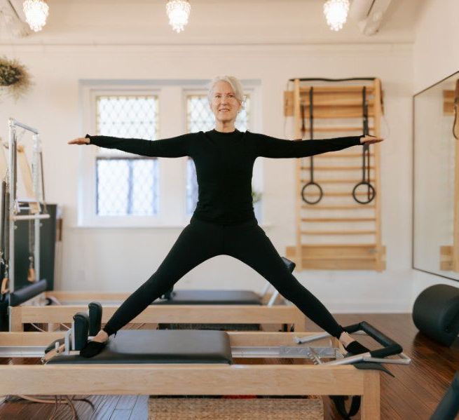 A woman is standing on a pilates machine with her arms outstretched.