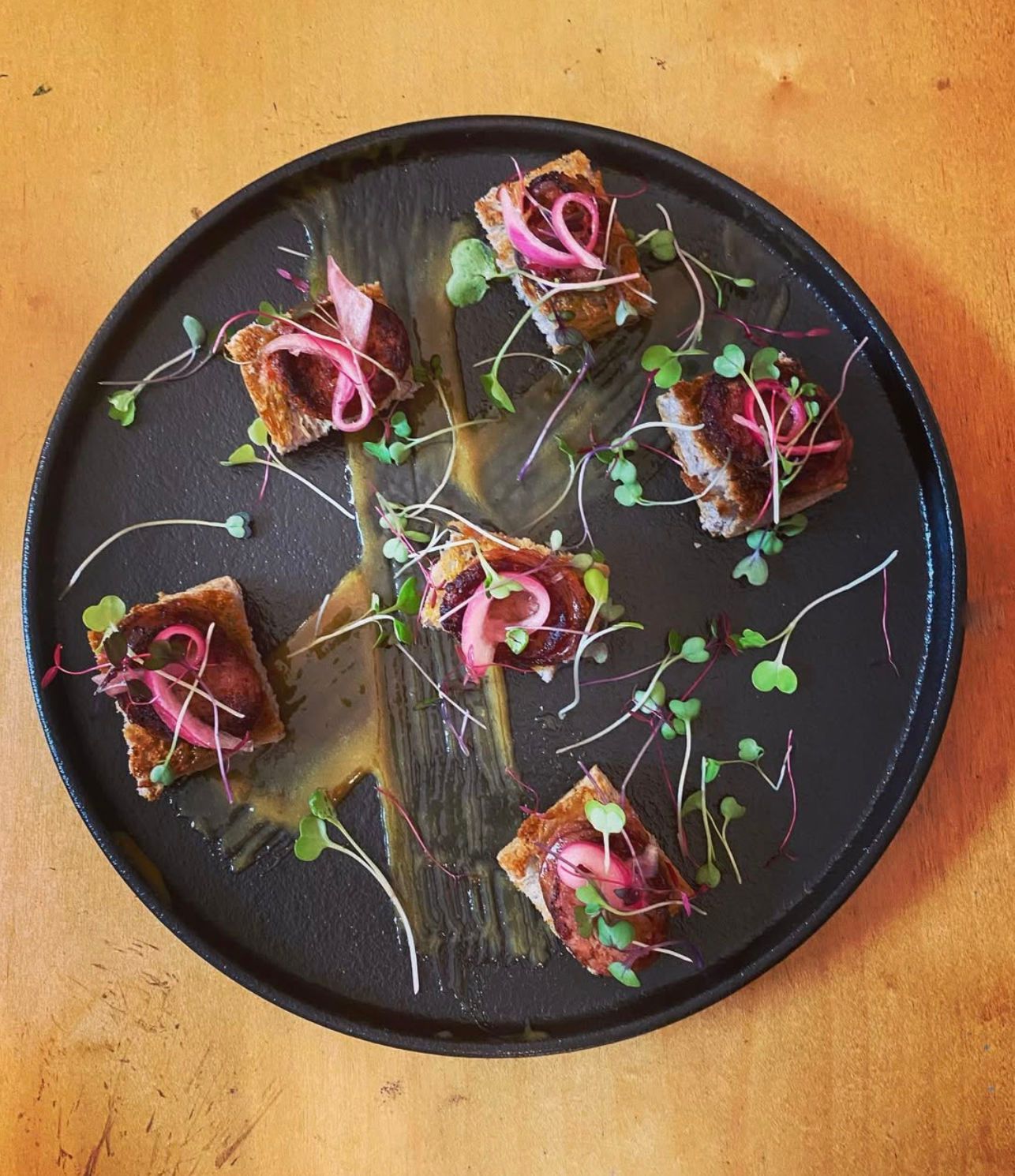 Black plate with five small colorful appetizers, garnished with microgreens on a wooden table.