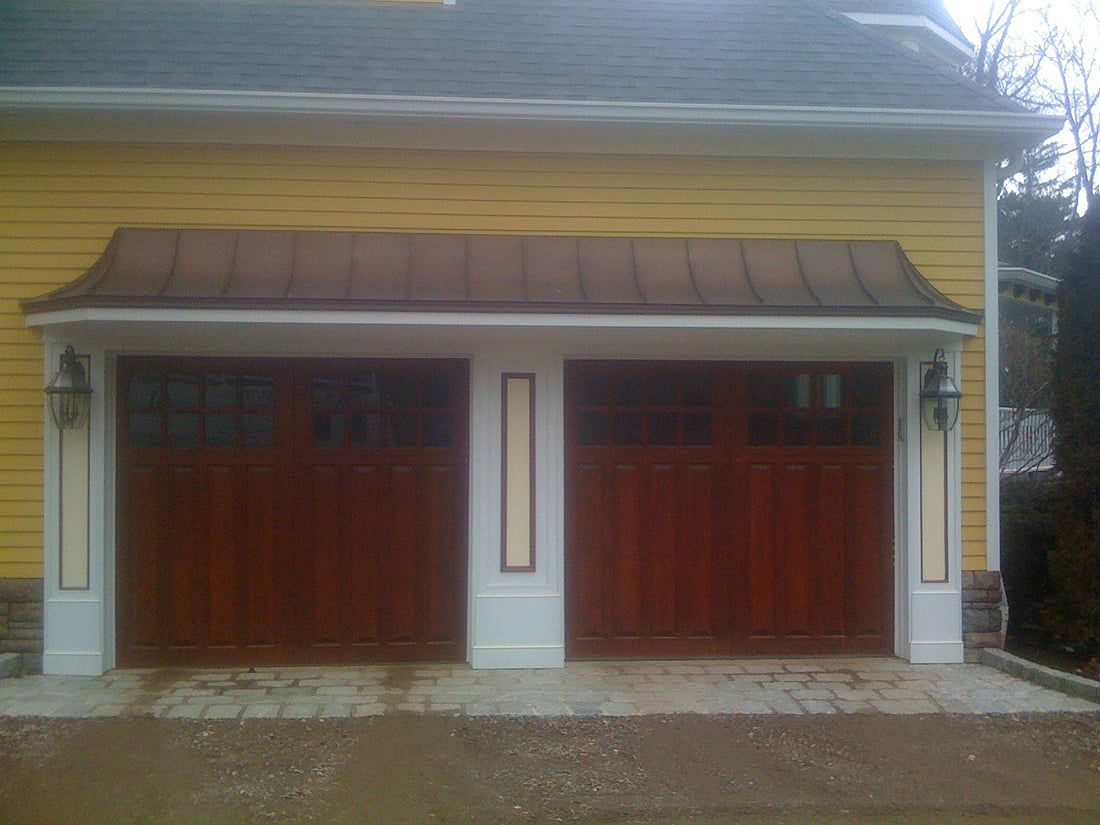 Two-car wooden garage doors under a brown metal awning on a yellow house