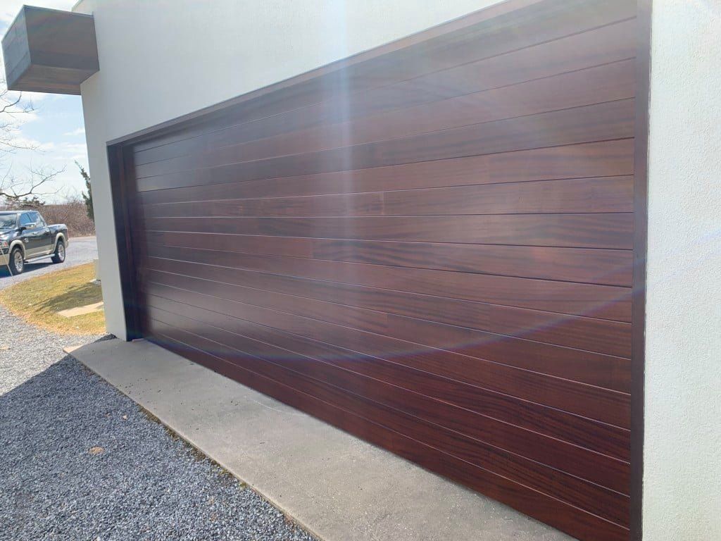 Dark wood-paneled garage door on a modern house exterior with concrete driveway and gravel border