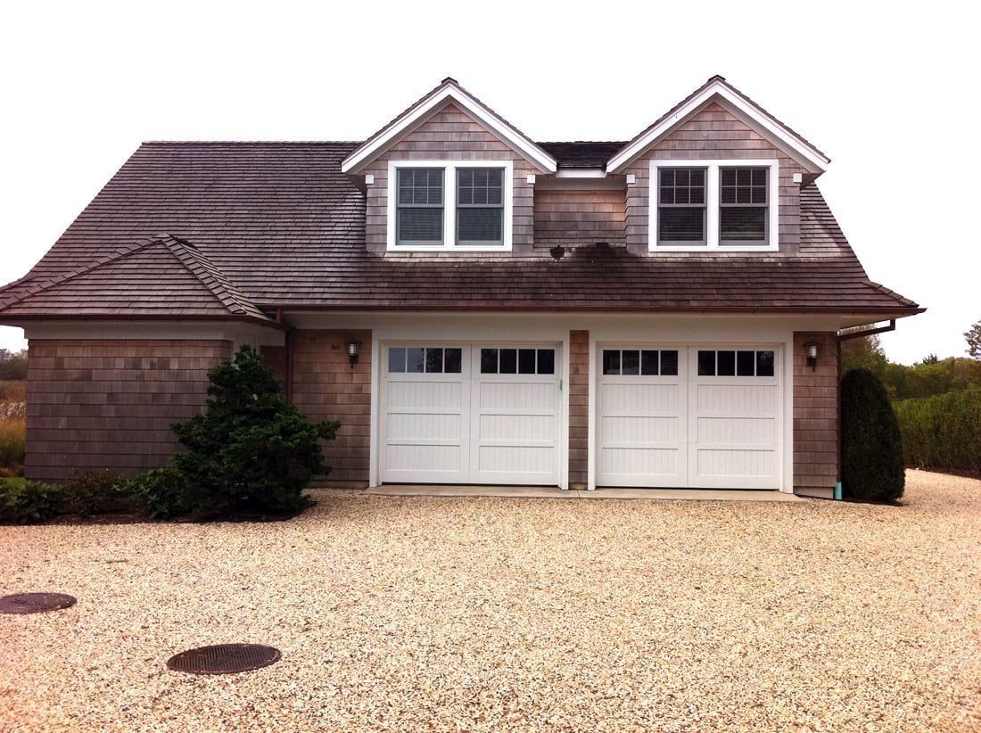 Suburban house with two white garage doors, brown shingled roof, and a gravel driveway