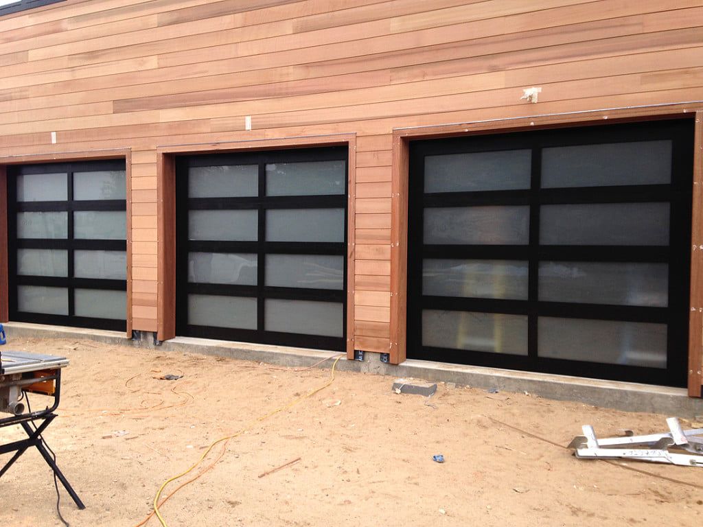 Three black garage doors set in a wooden exterior wall with a dirt foreground