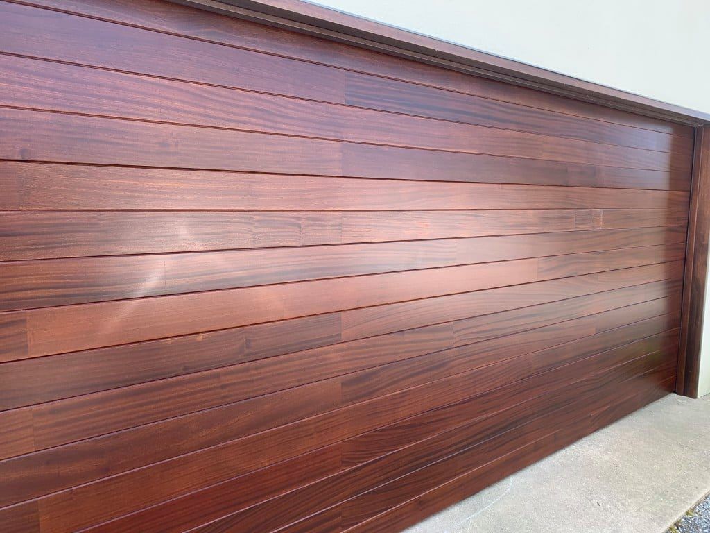 Brown wooden garage door with horizontal panels and a speckled concrete driveway.