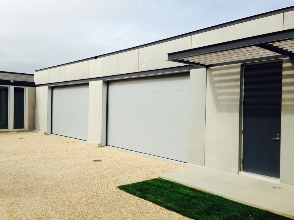 Modern row of white garage units with closed doors and a gravel driveway, plus a dark entry door