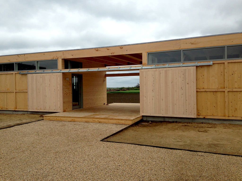 Partially built wooden building with open doorway and unfinished walls on a gravel lot under a cloudy sky