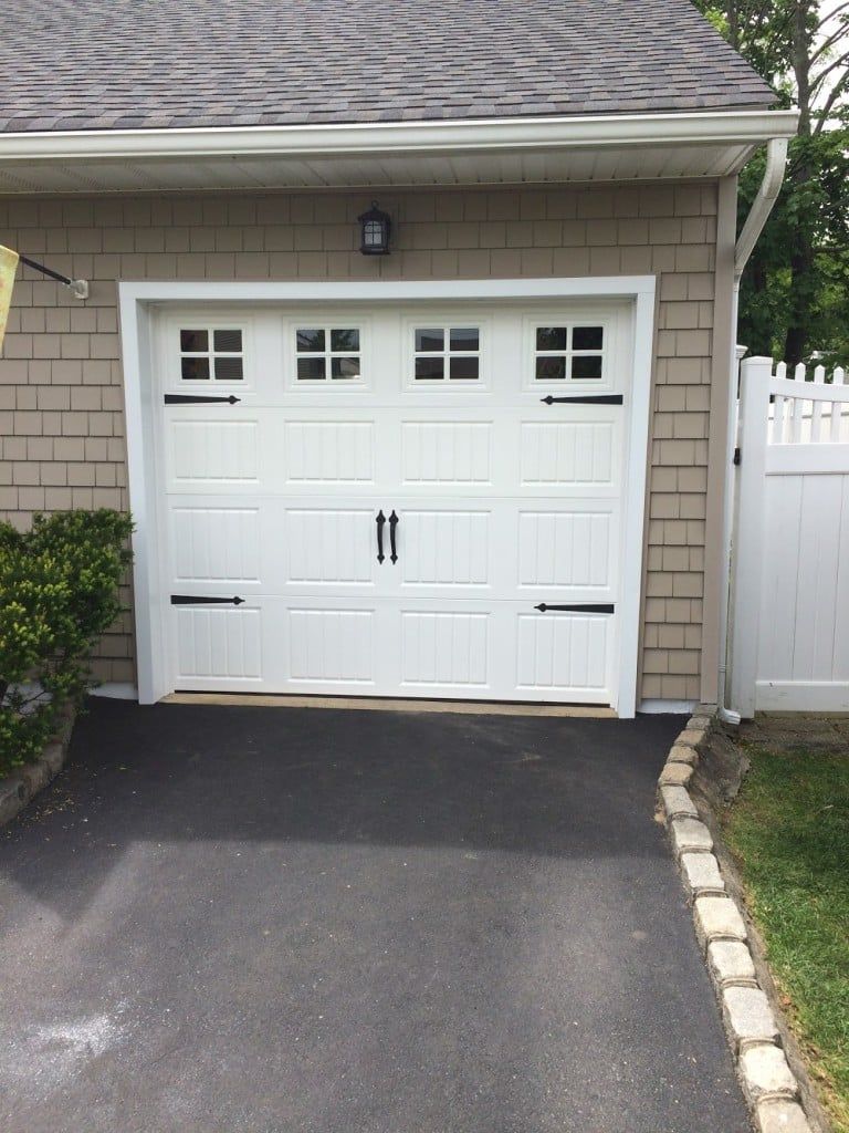 White garage door with small windows on a driveway beside a house exterior