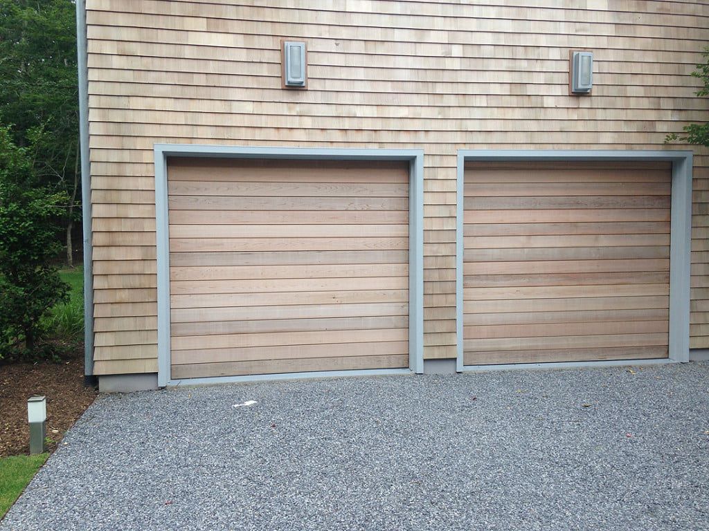 Two wood garage doors in a tan brick wall with gray trim beside a gravel driveway.