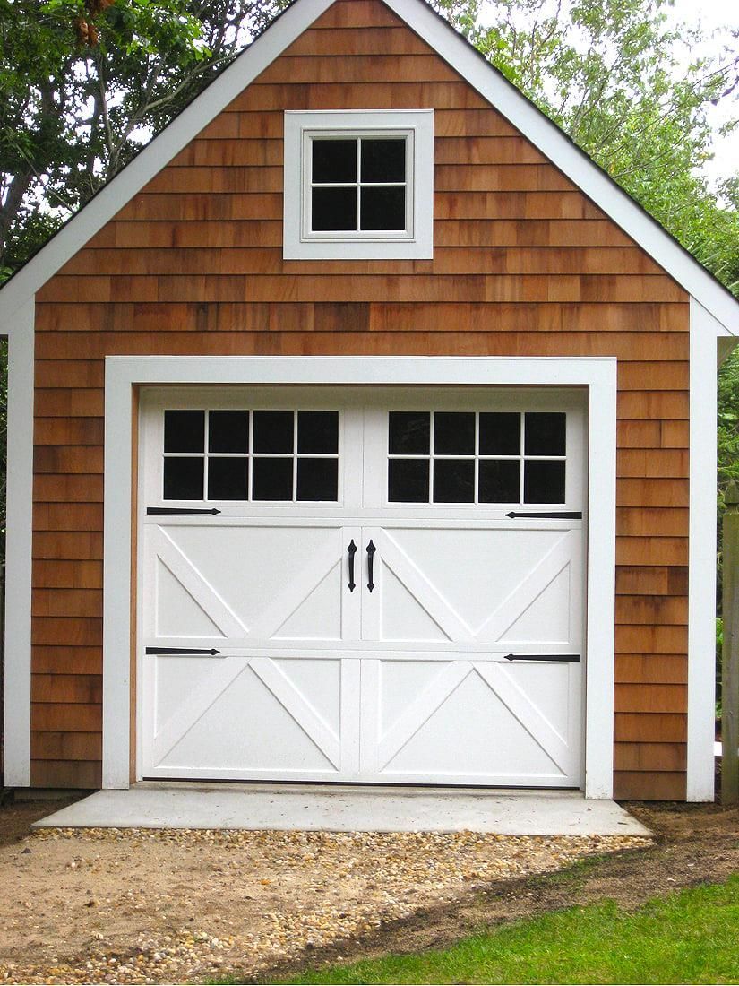 White garage door on a brown shingled shed with a small window above it