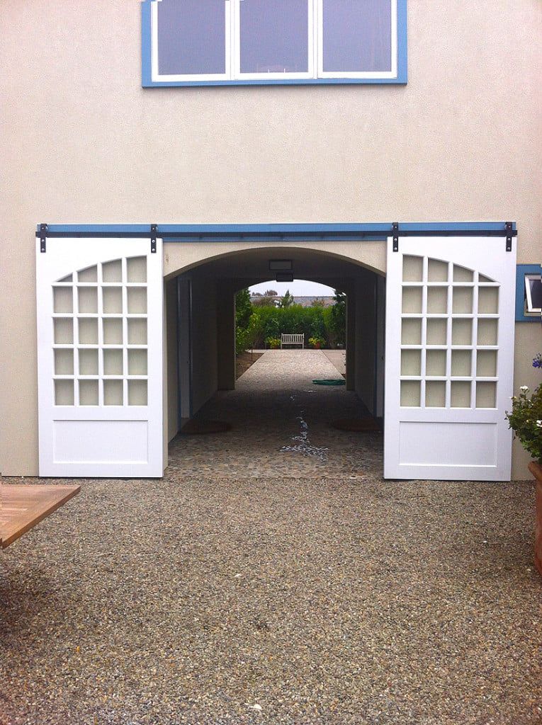 White double doors with glass panes open to a gravel courtyard and arched passageway.