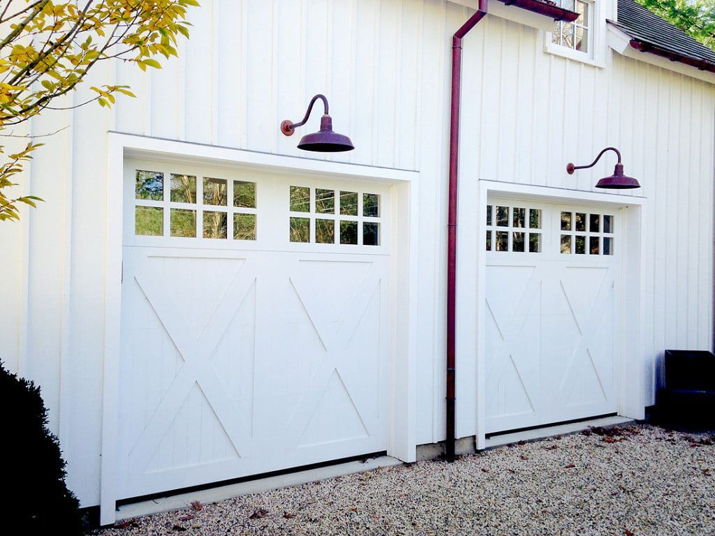 White garage doors with small windows on a white building, lit by purple exterior lamps, on a gravel driveway