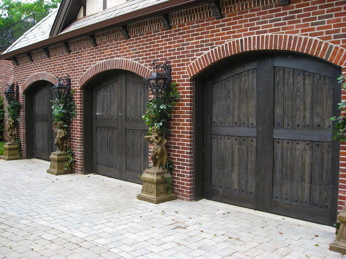 Brick building with three dark wooden arched doors along a paved driveway