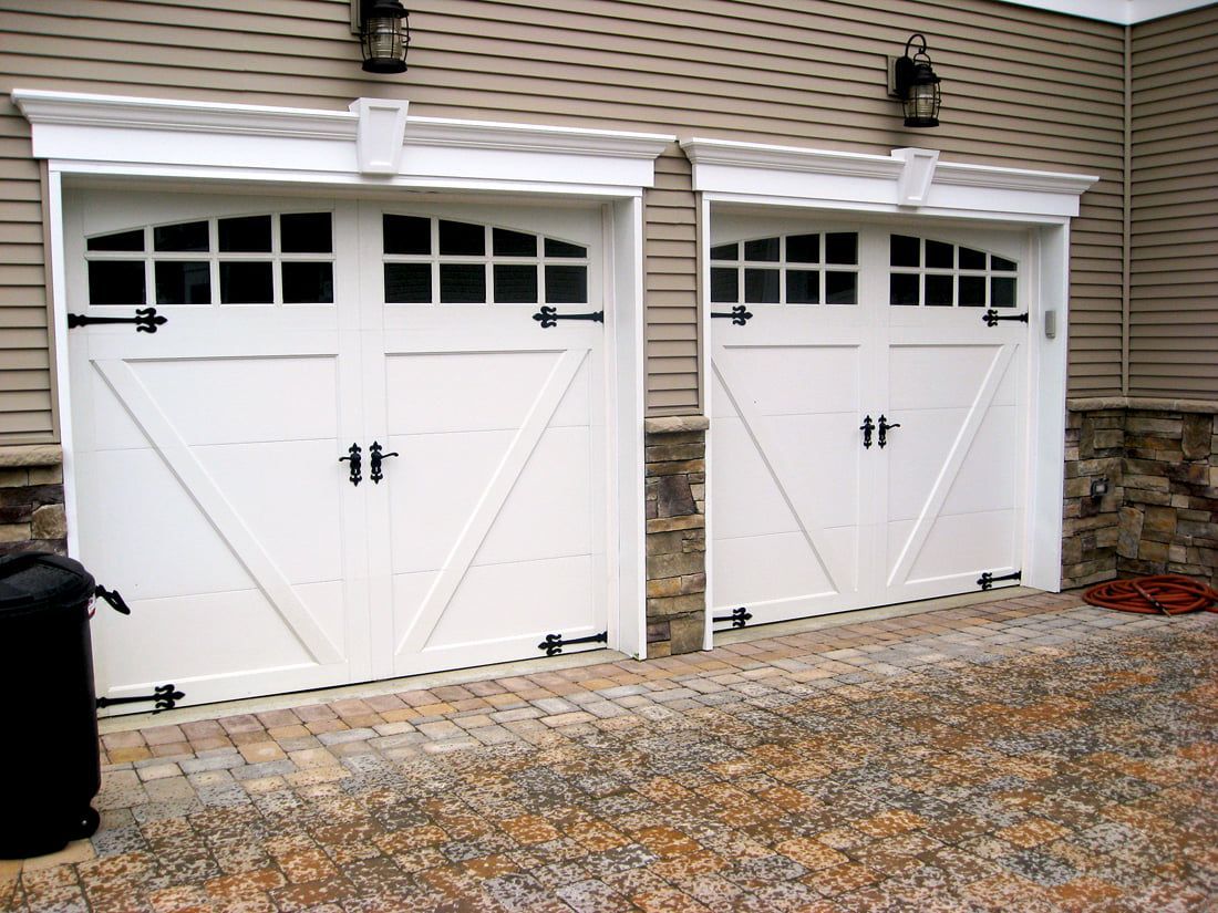 Two white garage doors on a stone-and-siding house with a paved driveway in front