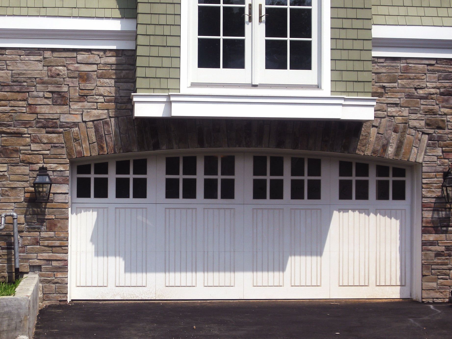 Stone house front with white garage door and a window above it