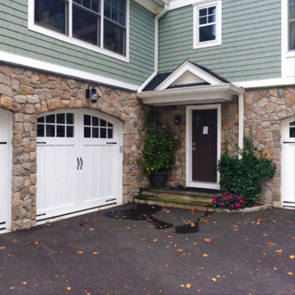 House exterior with stone facade, white garage door, front entry, and driveway.