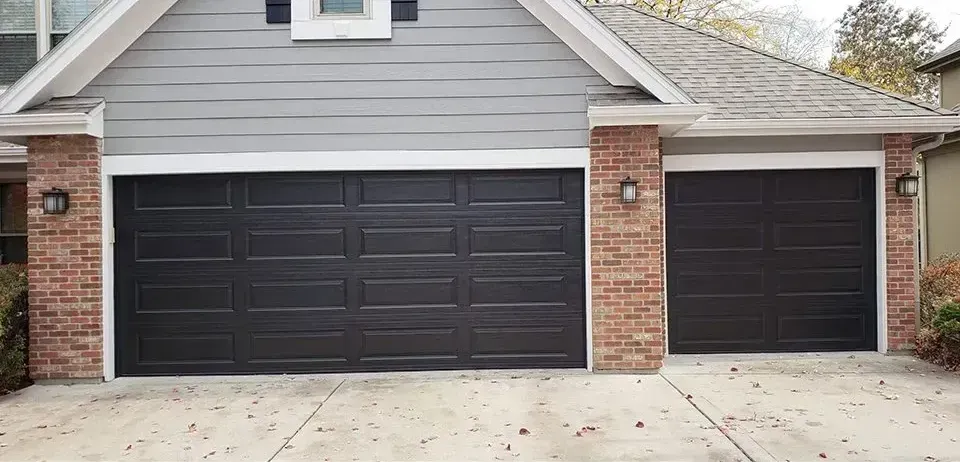 A house with two black garage doors and a brick wall.