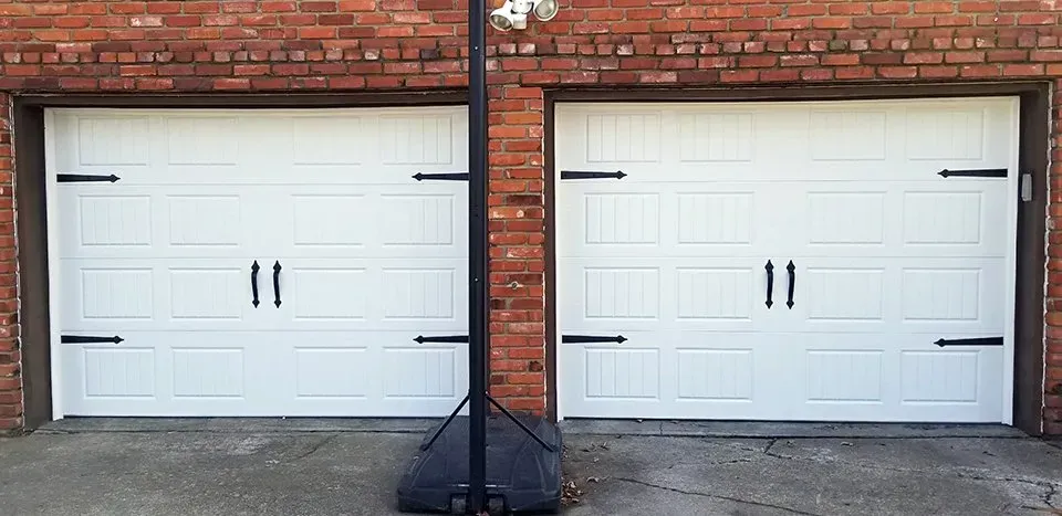 Two white garage doors next to a brick wall