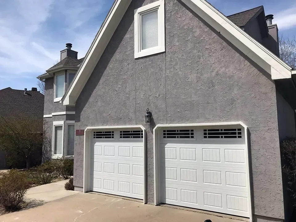 A gray house with two white garage doors and a window.