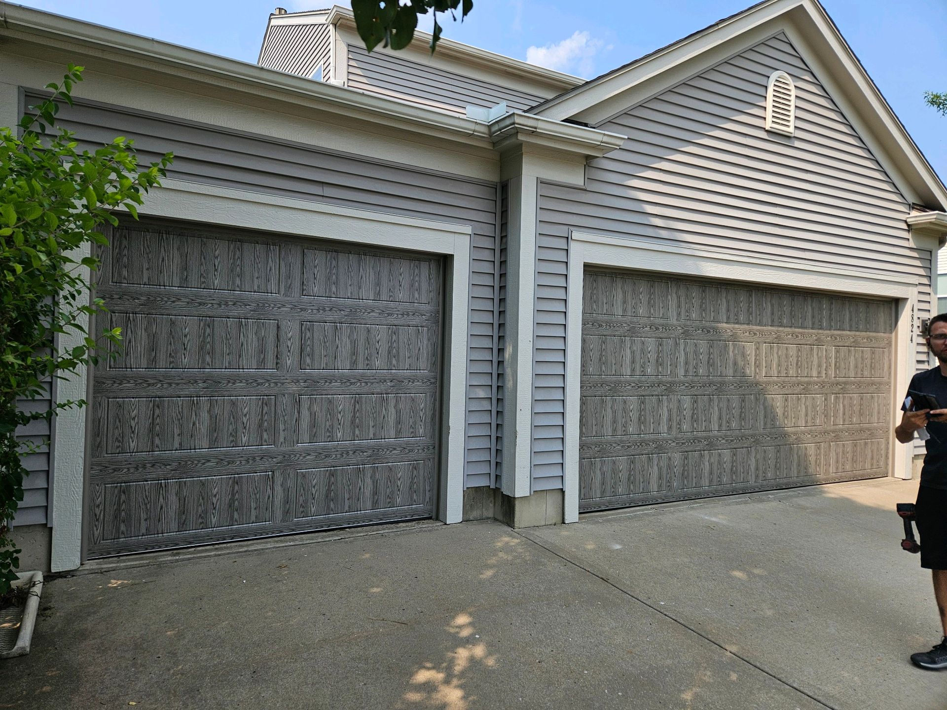 A man is standing in front of a house with two garage doors.