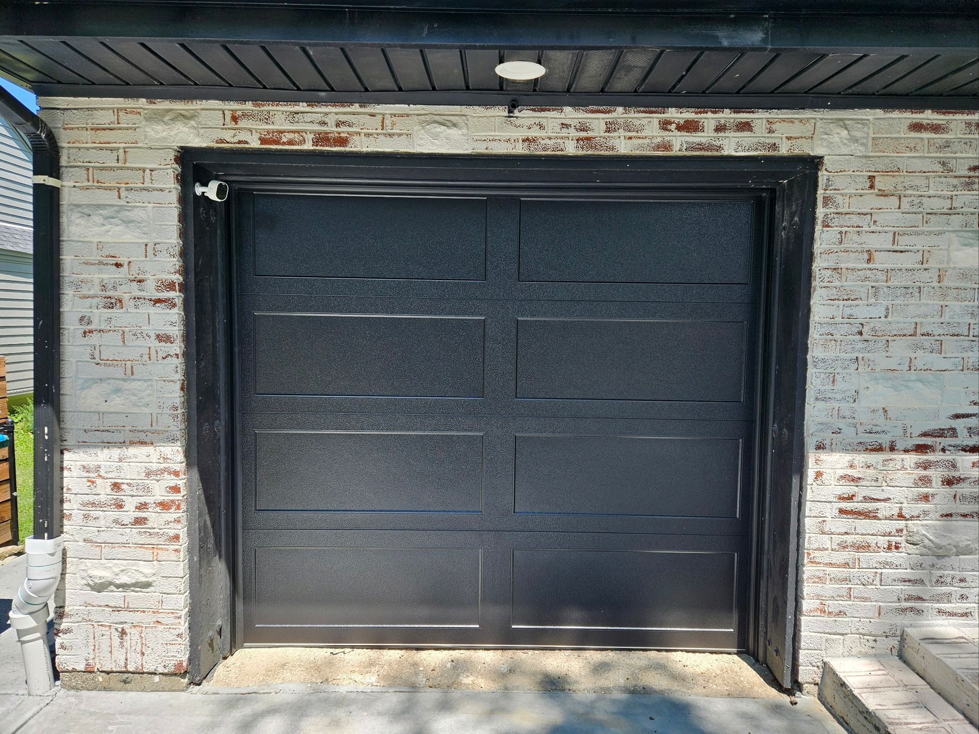 A black garage door is sitting on a white brick wall.