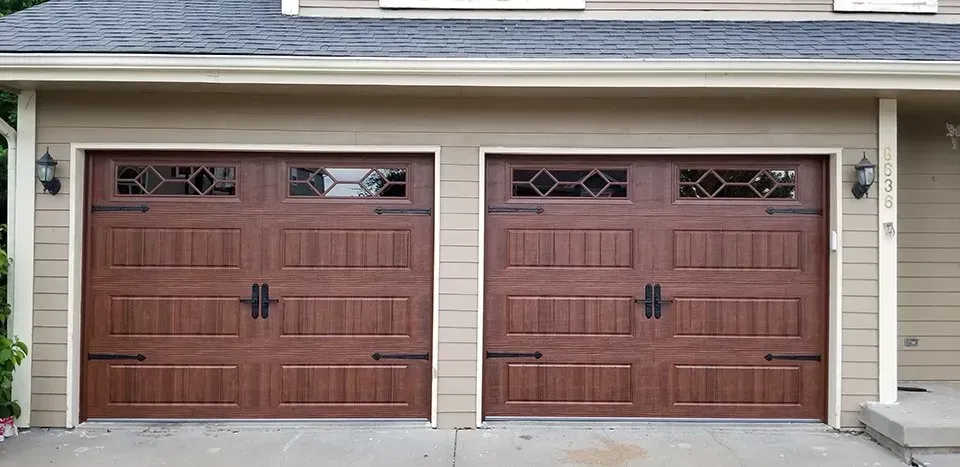 A house with two wooden garage doors in front of it.