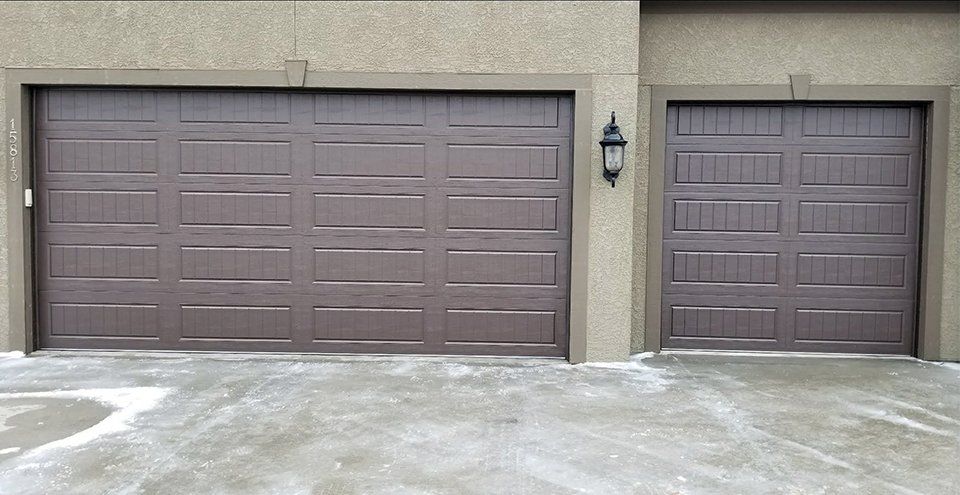 Two brown garage doors with a lamp on the side of the building
