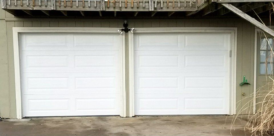 A pair of white garage doors are sitting next to each other on the side of a house.