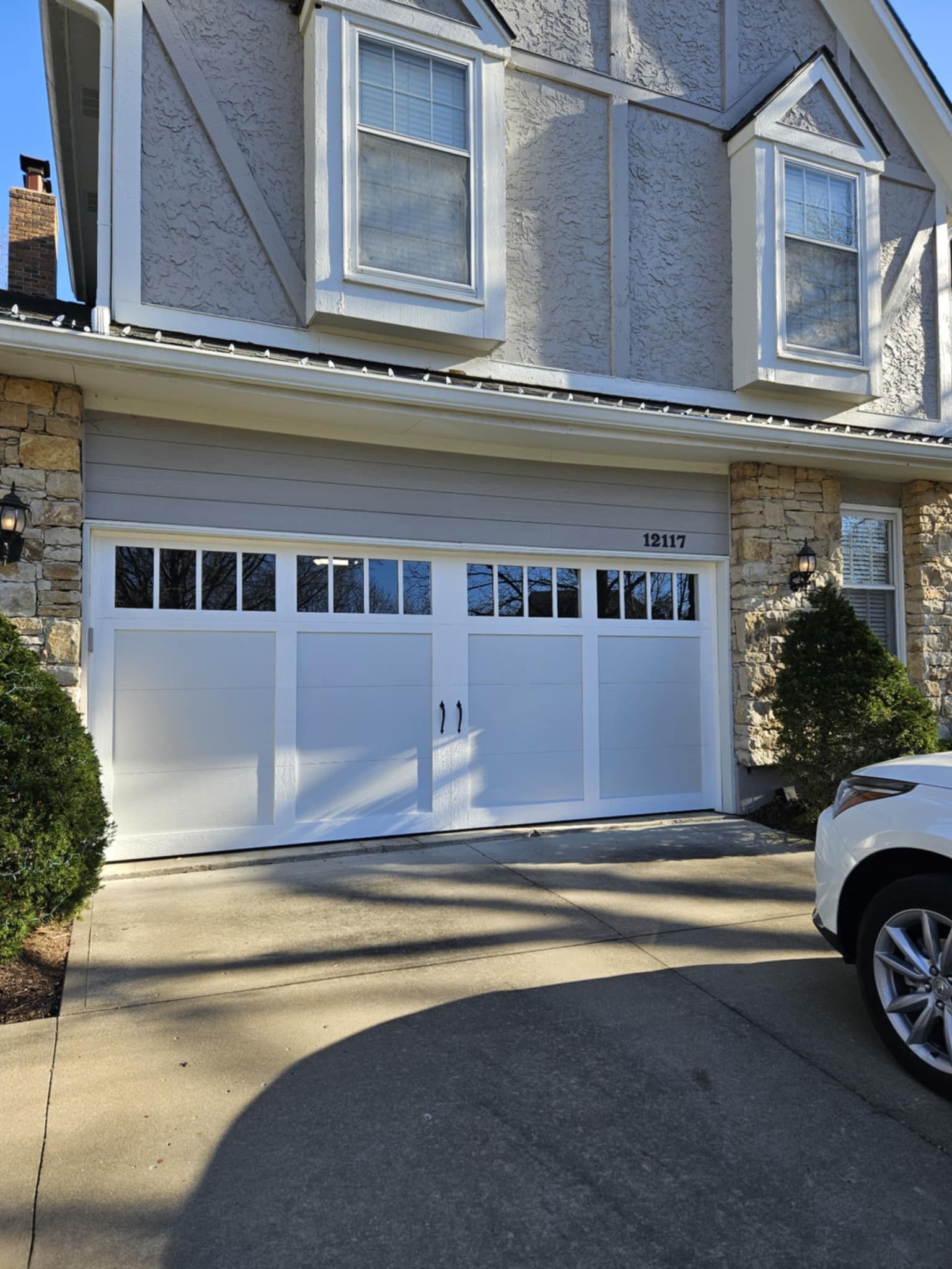 A white car is parked in front of a large white garage door.